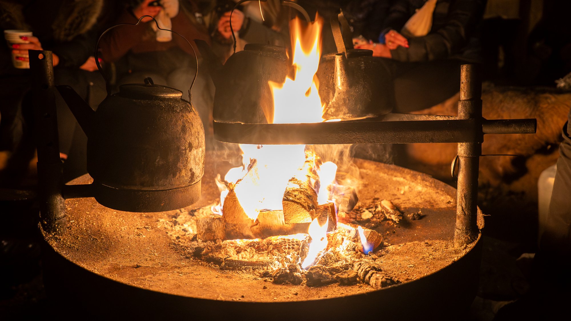 Kota 帐篷中央的火堆上，几只黑色水壶静静地煮着 Glögi