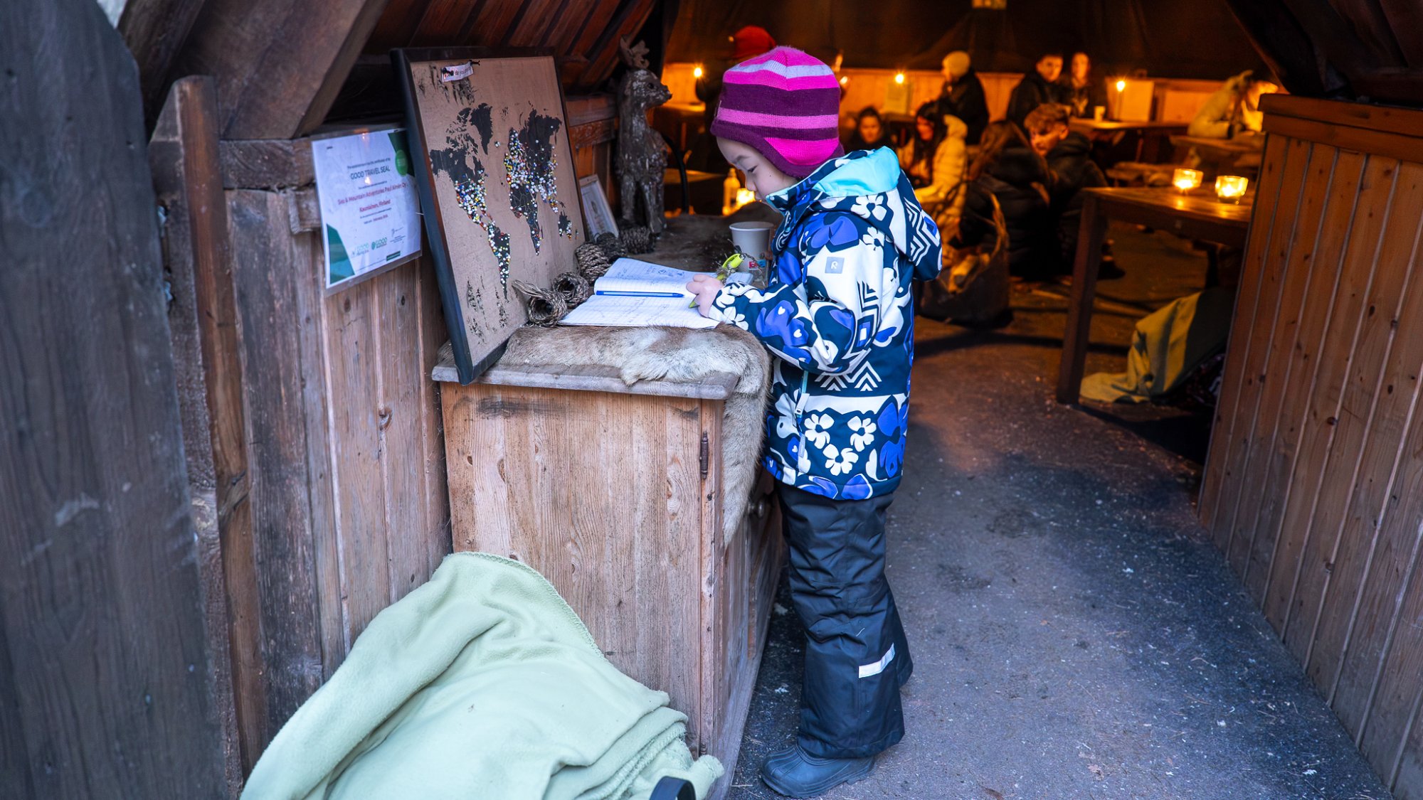 帐篷入口处，小朋友认真地在留言本上写下自己的痕迹，周围是安静而温暖的冬日氛围